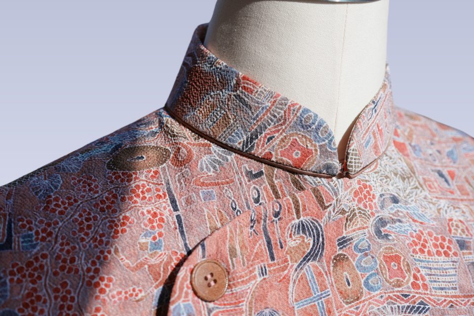 Pink sleeveless Qipao in Chirimen silk with an Egyptian wall painting motif, chocolate brown single rope piping under the collar and coconut shell buttons